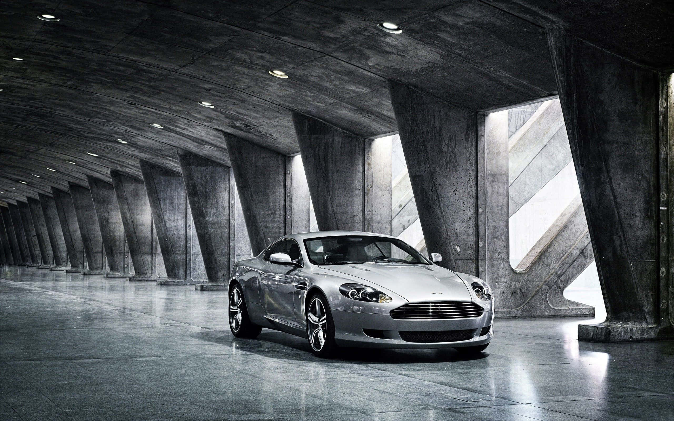 Aston Martin DB9 крузиращ през живописен градски пейзаж Тапет