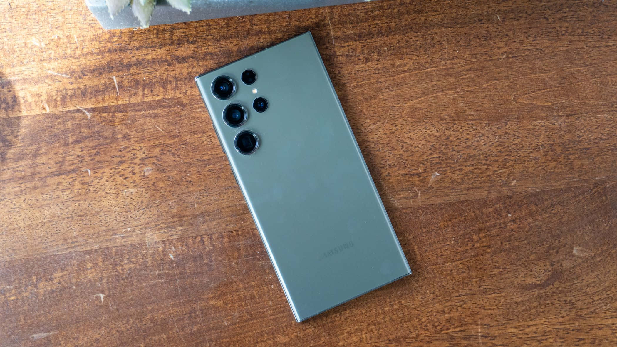 Samsung S23 Ultra зелен гръб с камери на дървена повърхност Тапет