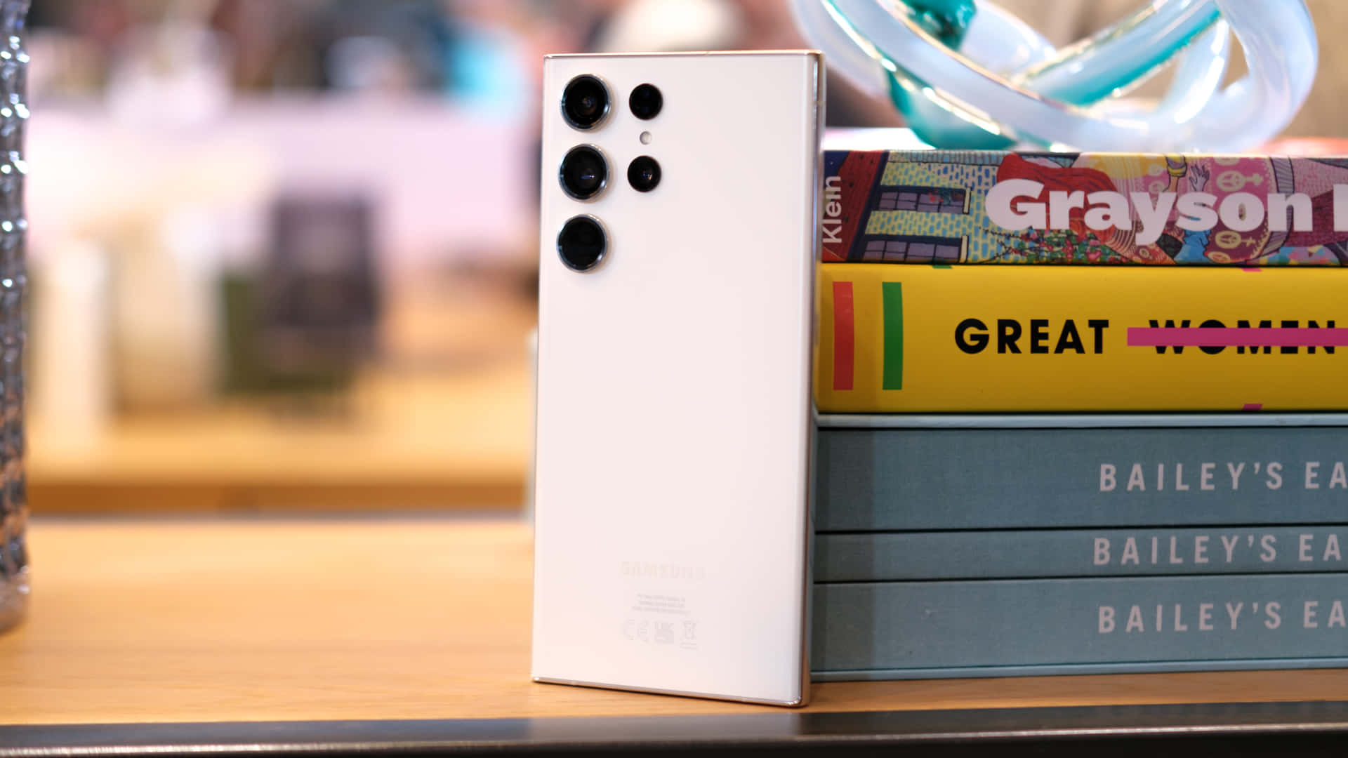 Samsung S23 Ultra в кремав цвят на фона на подредени книги Тапет