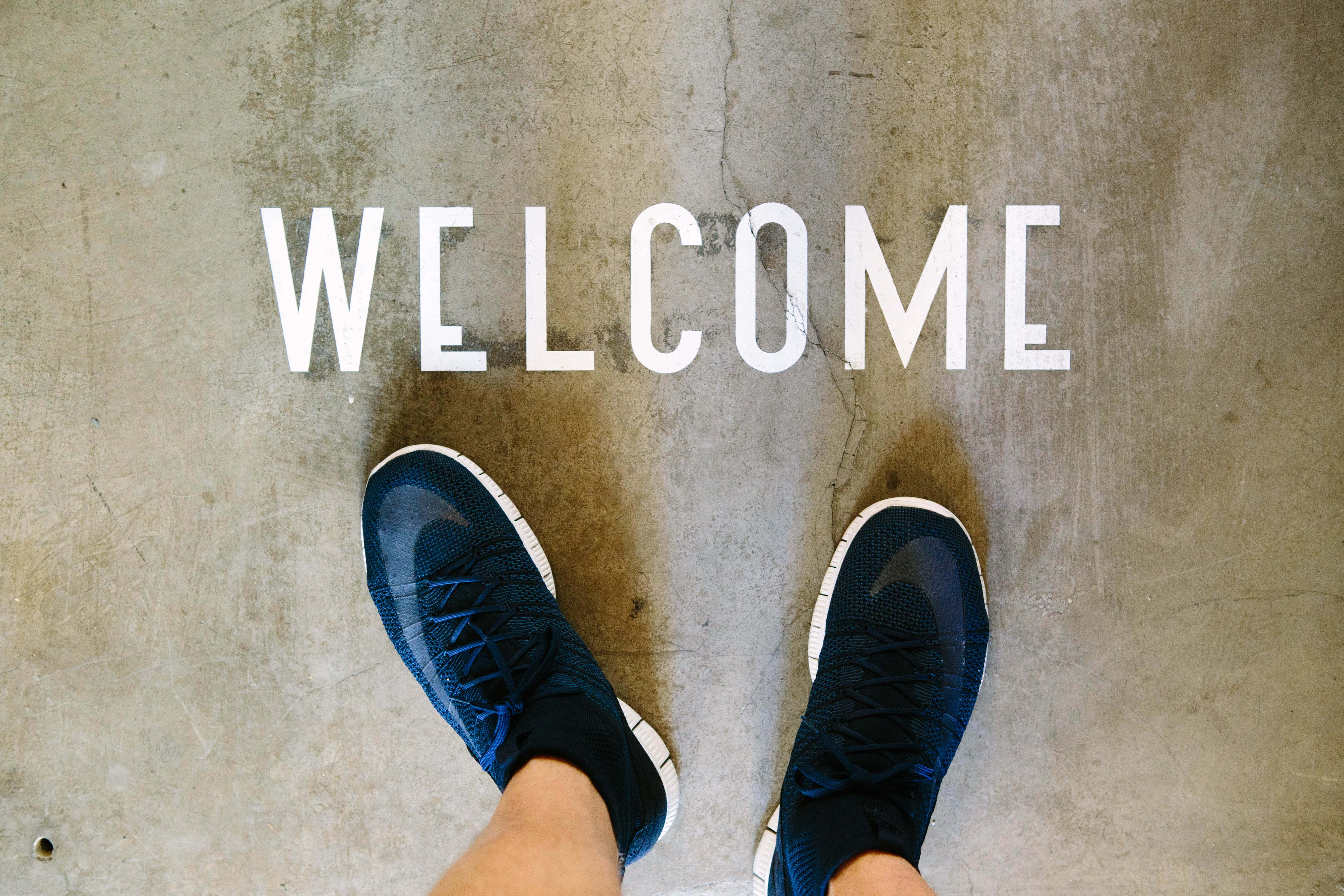 Човечи крака, стоящи на бетонен под с надпис welcome Тапет