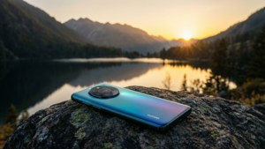 Телефон Huawei на скала с изглед над планинско езеро при залез слънце, спокойна природа.
