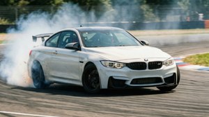 Бял BMW M4 дрейфира в завой на писта с димен следи от гуми и замъкване на движението. — BMW Тапет