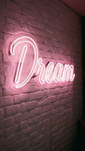 Светло-розова неонова надпис 'Dream', коя свети на бяла тухлена стена, вдъхновяща и естетична. — Светло розова естетика Тапет